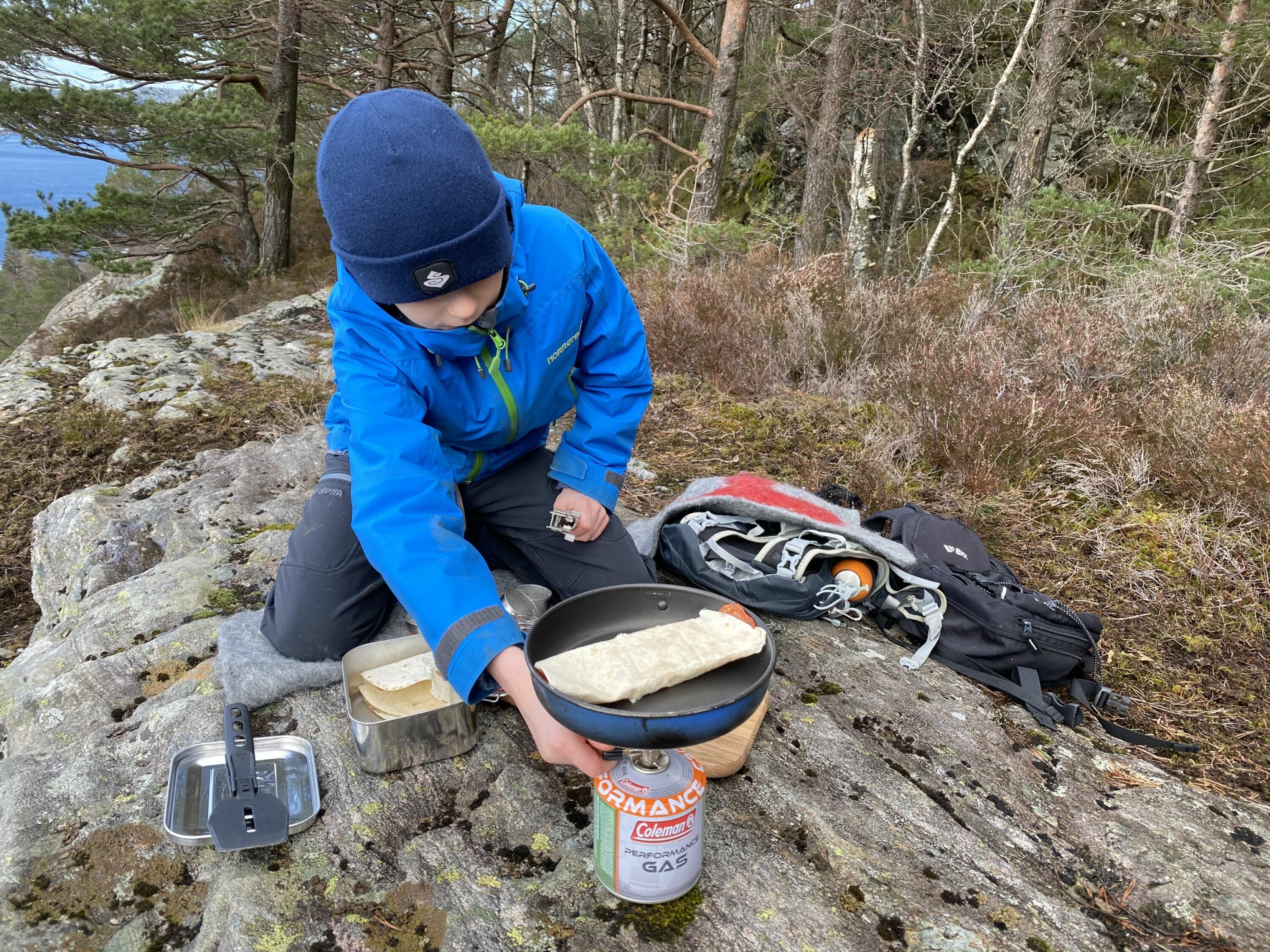 En gutt lager mat på primus i skogen.